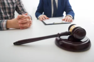 A lawyer sitting beside a client with files and a gavel on the table.
