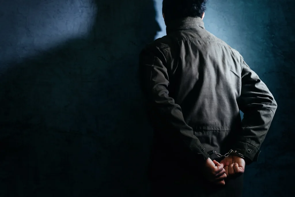 A man facing a wall with his hands behind him with handcuffs.